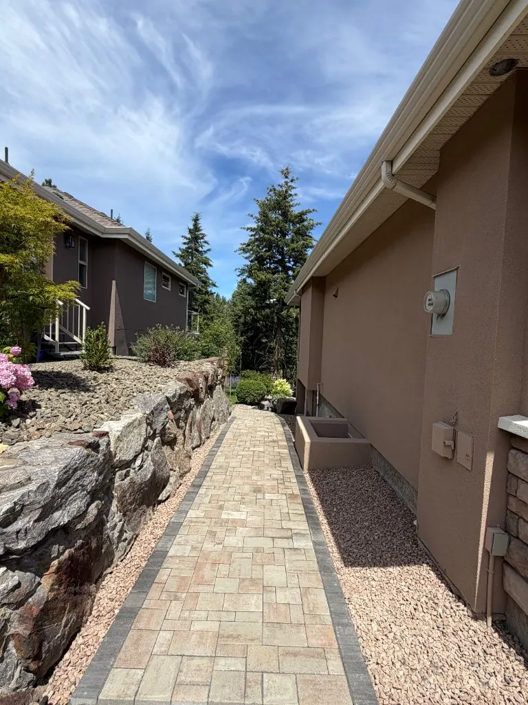 Interlocking stone walkway beside a natural rock retaining wall and garden beds